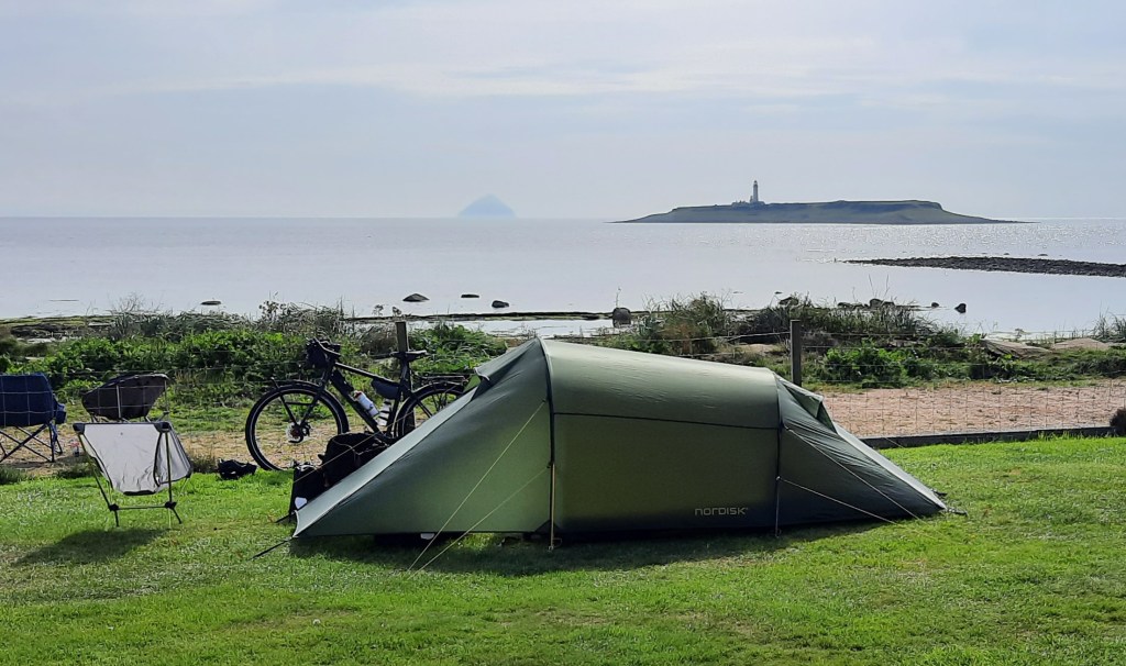 Green tent with bicycle behind it. Scene looking out over sea with island.
